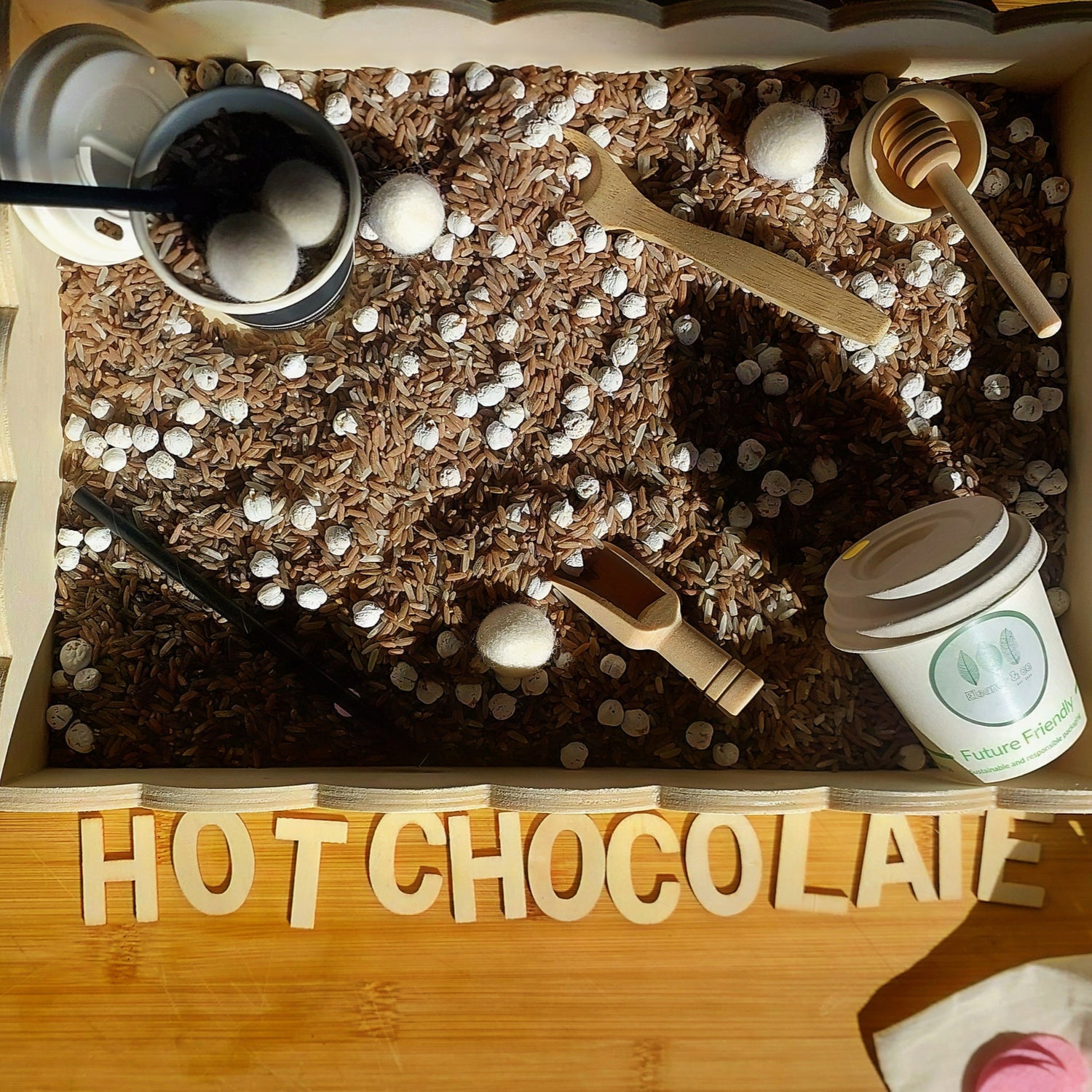 Hot chocolate station with cocoa, milk, and a small cup on a wooden surface.